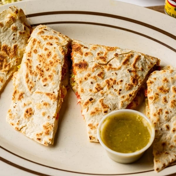 Four quesadilla slices with lettuce and tomato, served with green salsa on a white plate.