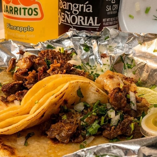 Three street tacos with meat, onions, cilantro, and lime, alongside Jarritos and Sangria Señorial sodas.