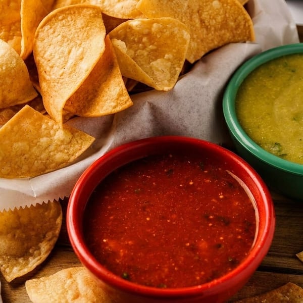 Crispy tortilla chips in a basket with red salsa and green salsa in colorful bowls.